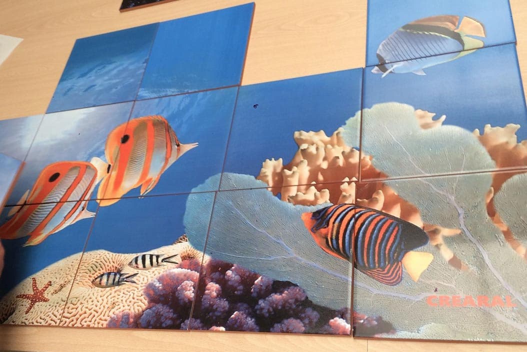 Mural cerámico de peces tropicales repartido en piezas sobre la mesa del taller