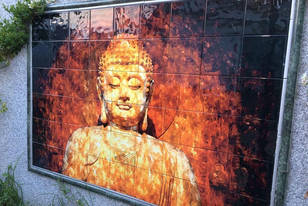 Mural cerámico de un Buda en una pared exterior, con cenefa verde