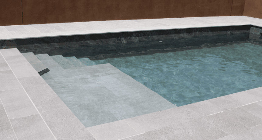 Piscina con coronación, playa y escalera en porcelánico gris claro