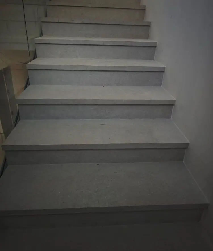 Escalera de obra con huella y tabica de porcelánico gris y barandilla de cristal, recién colocada
