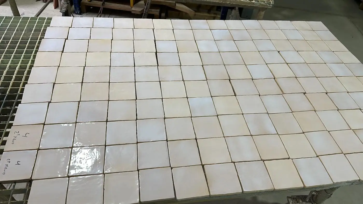 Piezas blancas esmaltadas a mano, de borde irregular, sobre la mesa del taller