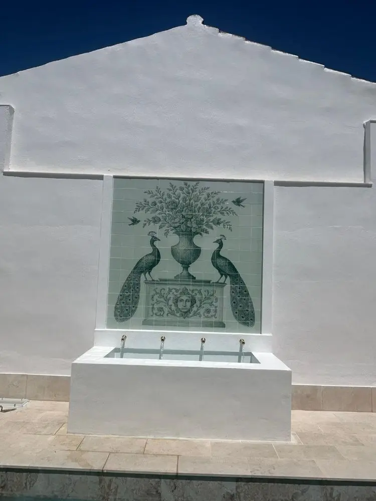 Mural cerámico de pavos reales instalado en una fachada, sobre una fuente