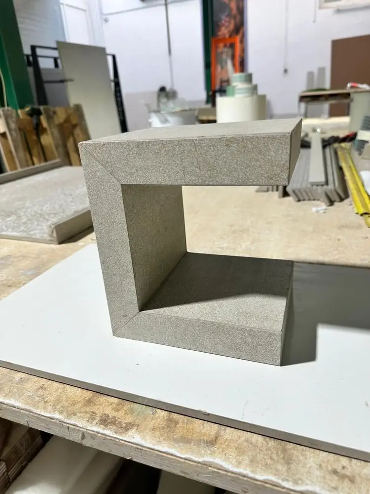 Pieza de porcelánico gris con tres caras unidas a inglete en forma de U, sobre la mesa del taller