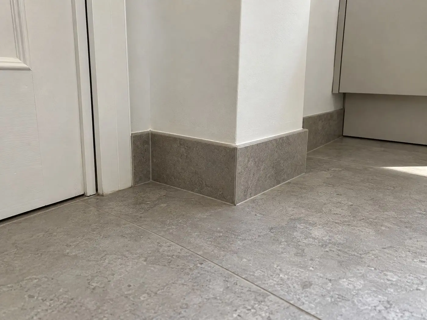 Rodapié de porcelánico gris efecto piedra, del mismo material que el suelo, rodeando un pilar