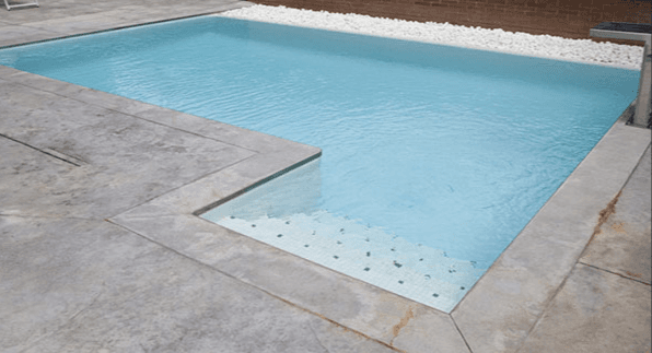 Esquina de una piscina con borde y playa de piezas grises efecto piedra