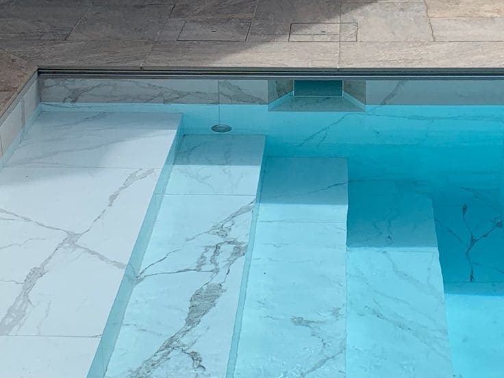 Peldaños y banco dentro de una piscina, en porcelánico blanco efecto mármol