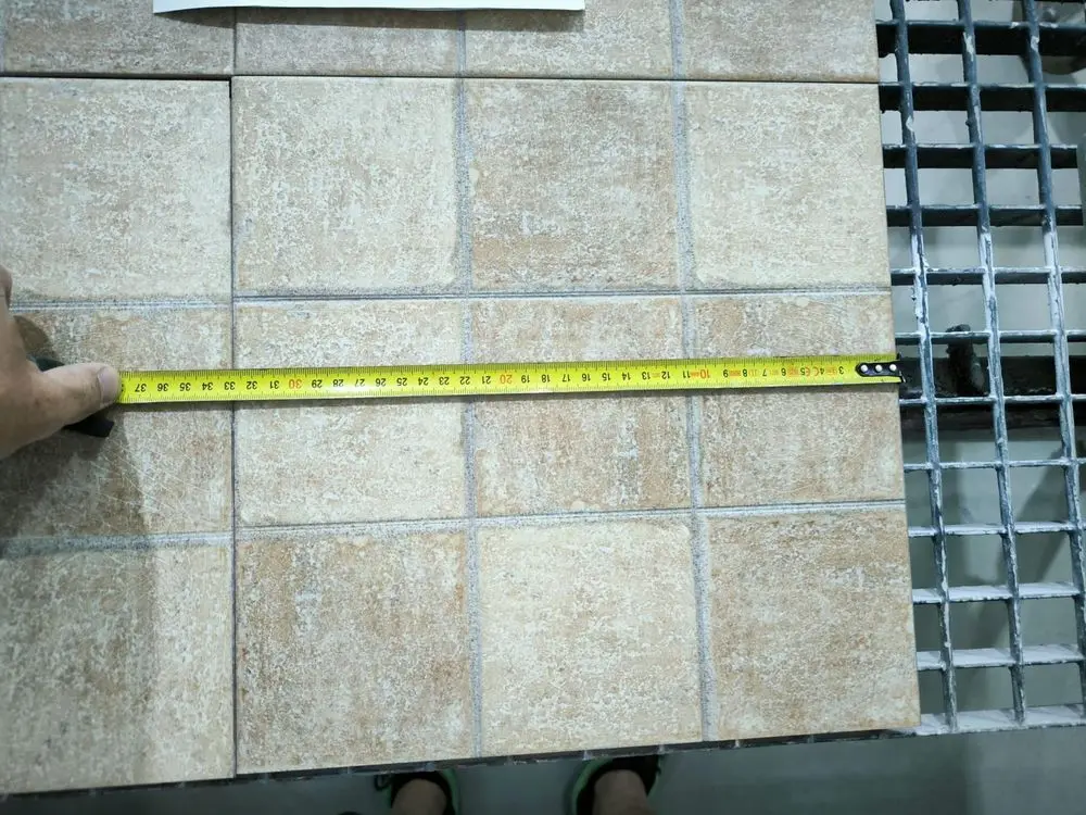 Baldosas beige jaspeadas medidas con cinta métrica sobre la mesa del taller