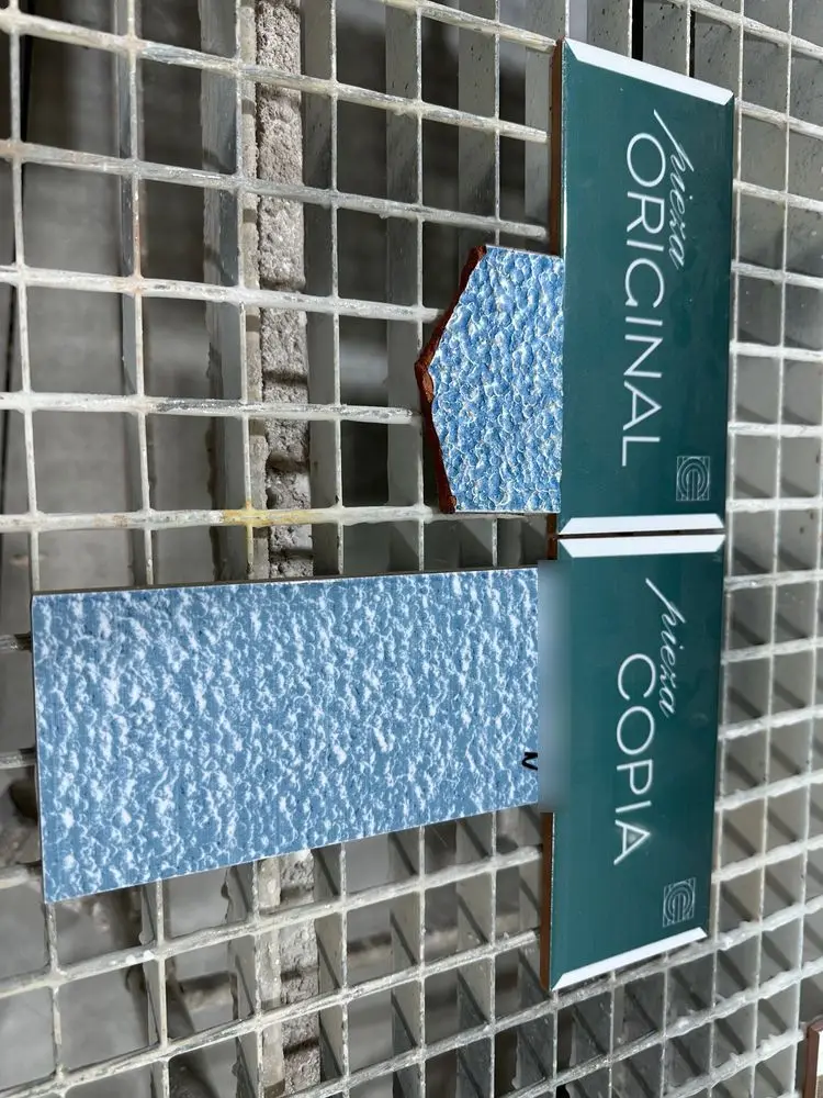 Trozo roto de un azulejo azul con relieve y su copia, con los carteles de pieza original y copia