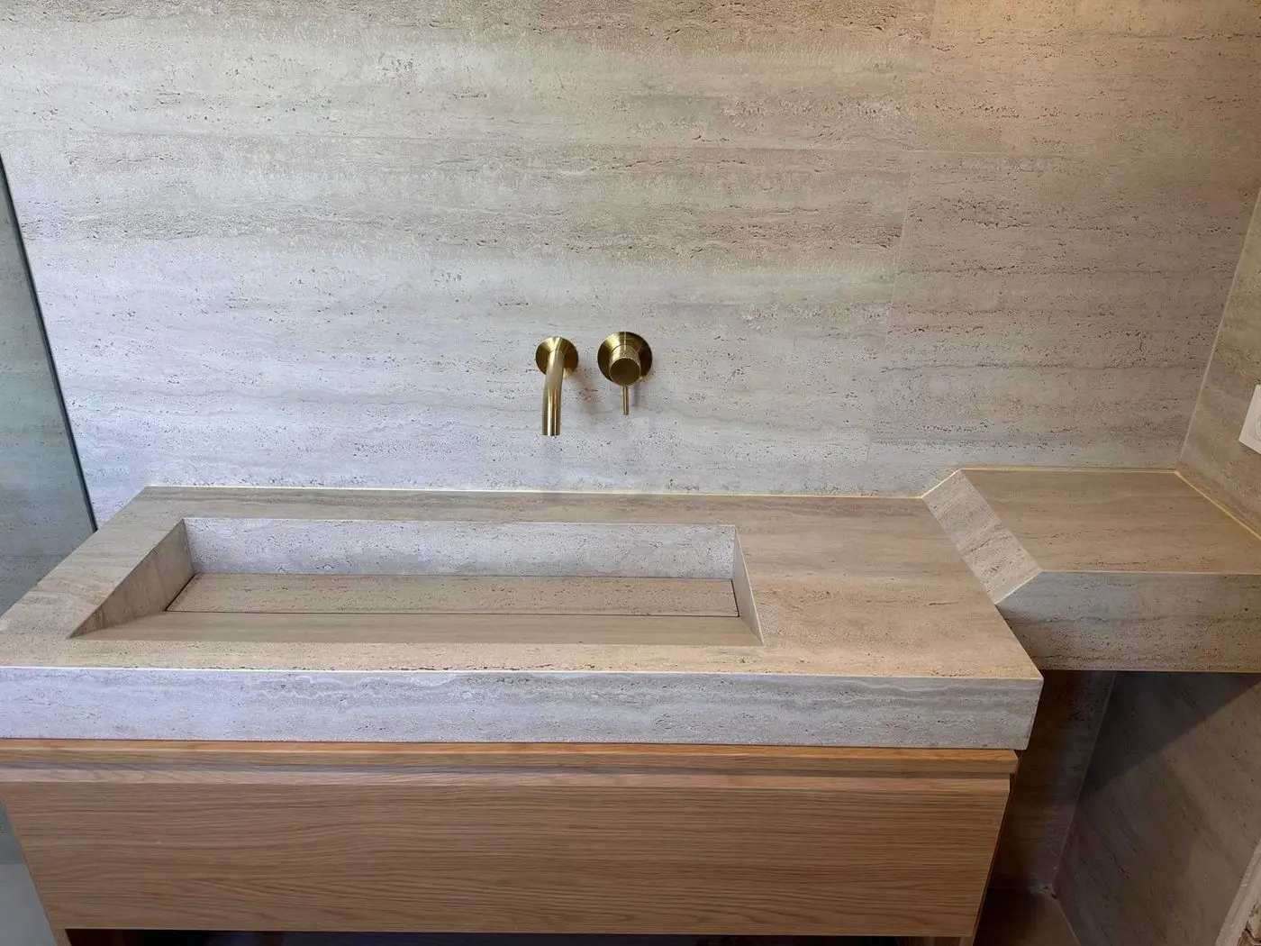 Seno integrado de porcelánico efecto travertino con el fondo en pendiente y grifería empotrada dorada